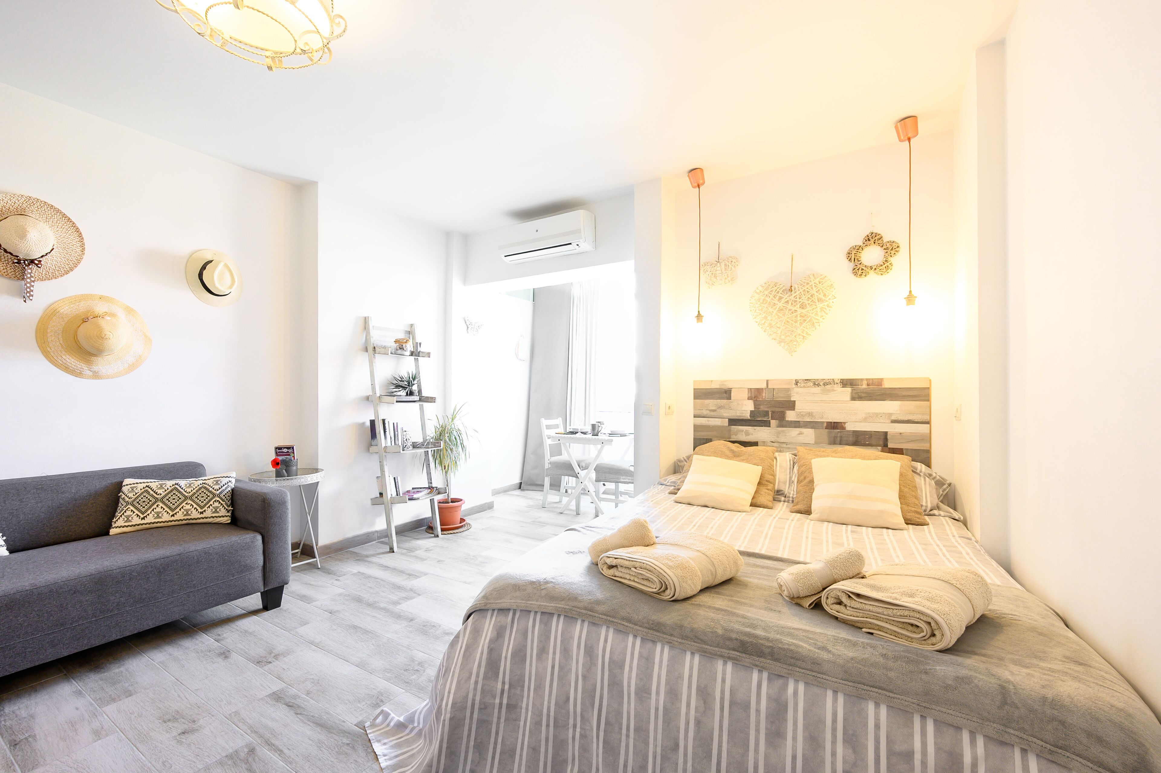 A modern hotel room with a grey sofa, a neatly made bed with striped bedding, and a small table with a potted plant.