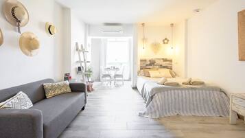 Ein modernes Hotelzimmer mit grauem Sofa, einem Bett mit gestreifter Bettwäsche und einem kleinen Nachttisch.