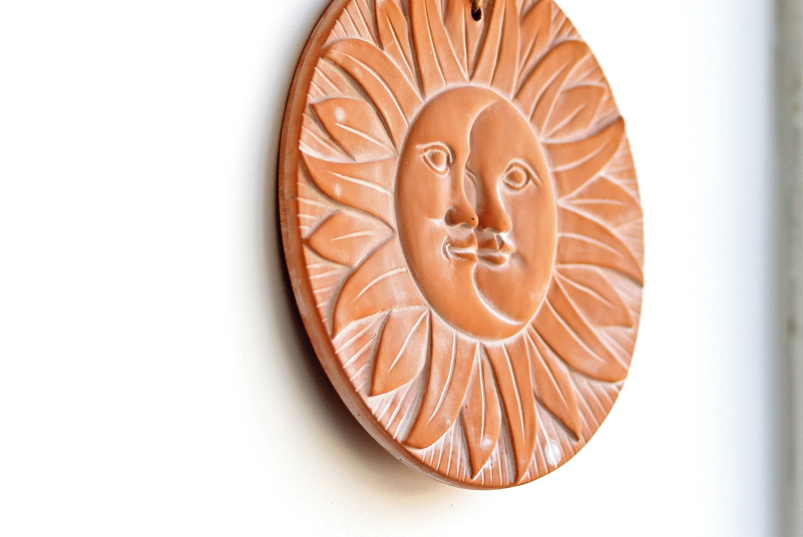 A ceramic wall decoration with a sun and face design.