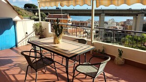 Eine Terrasse mit Tisch und Stühlen, einer Kakteenpflanze und Blick auf eine Brücke und Stadtlandschaft.