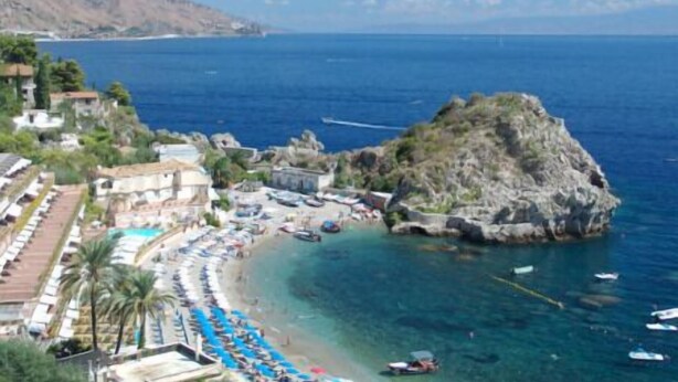 Ein Küstenhotel mit Strand, klarem blauen Wasser und felsigem Gelände.