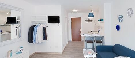 Una sala moderna con un sofá azul, un mueble blanco para el televisor y piso de madera.