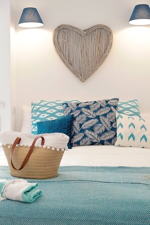 A neatly made bed with patterned pillows, a heart-shaped wall decoration, and a woven basket with a brown handle.