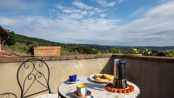 Ein Tisch mit einem Metallstuhl, einem Teller mit Essen, einer Tasse und einem Campingkocher auf einem Balkon mit schöner Aussicht.