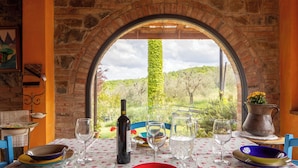 A table set for dining with a view through an arched window, a wine bottle, and a vase with flowers. - Il Poggio dell'Eremita (Sinalunga)