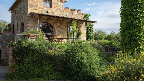 A stone building with a balcony, surrounded by lush greenery and flowering plants. - Il Poggio dell'Eremita (Sinalunga)