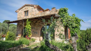 A stone house with a sloped roof, a wooden porch, and a garden with various plants and flowers. - Il Poggio dell'Eremita (Sinalunga)