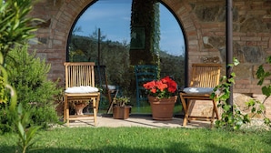 An outdoor seating area with two wooden chairs and a potted plant with red flowers. - Il Poggio dell'Eremita (Sinalunga)