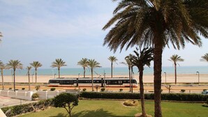A train station with a modern train, palm trees, and a beach in the background. - LOFT PLAYA MUCHAVISTA (El Campello)