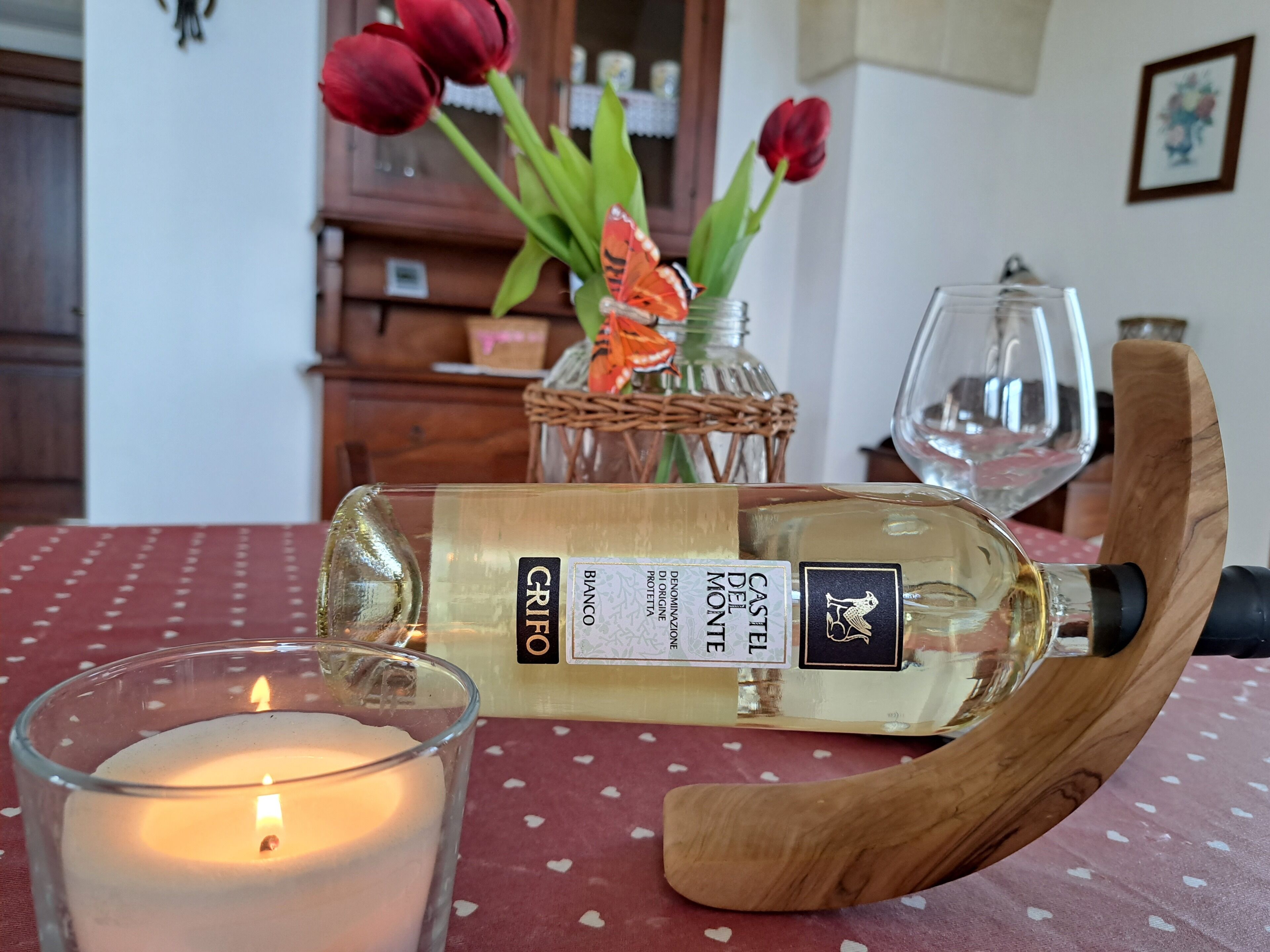 A bottle of Castello del Monte Progetto Proteina wine, a candle, and a glass of wine on a table with a red tablecloth.