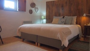 A bedroom with a bed, a window, a wall-mounted heater, and a lamp.