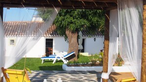 A covered outdoor area with a tiled floor, yellow lounge chairs, and a white building in the background.