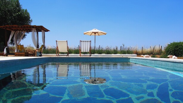 A clear swimming pool with a wooden pergola and two sun umbrellas.