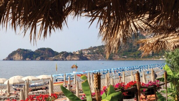 A beach with umbrellas and lounge chairs, a clear view of the sea, and a mountainous backdrop. - Holiday Apartment Da Rosa Studio (Letojanni)