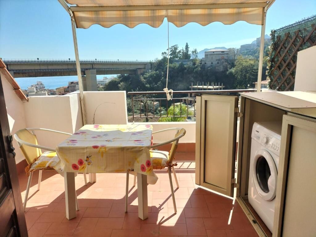 A balcony with a table and chairs, a washing machine, and a view of a bridge and buildings.