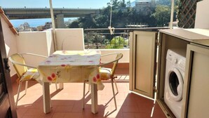 A balcony with a table and chairs, a washing machine, and a view of a bridge and buildings. - Holiday Apartment Da Rosa Studio (Letojanni)