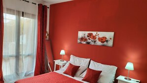 A bedroom with a red wall, a bed with white and red bedding, two bedside lamps, and a painting of flowers. - Holiday Apartment Da Rosa Studio (Letojanni)