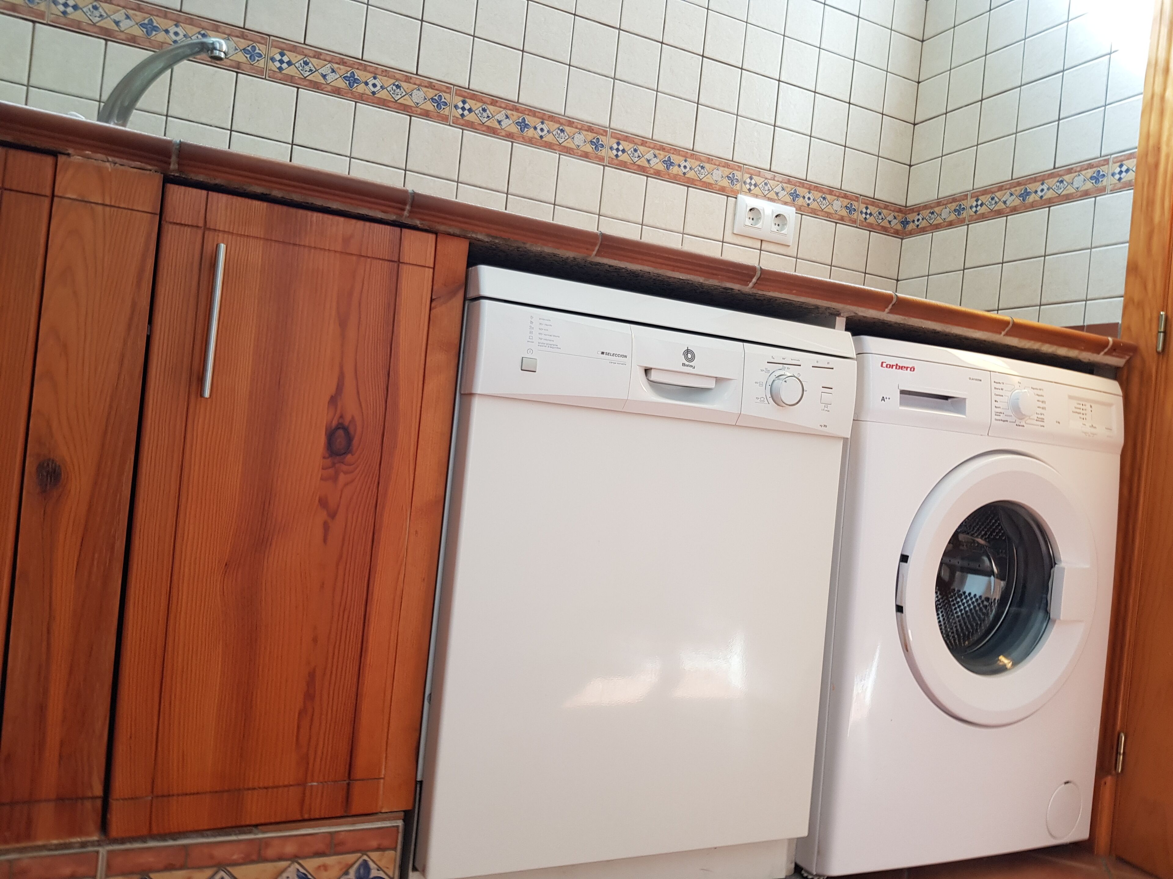A compact laundry area with a front-loading washing machine and dryer, wooden cabinets, and tiled backsplash.