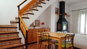 Een keuken met een houten trap, een eettafel met stoelen, een rode lamp en een zwarte kookplaat.