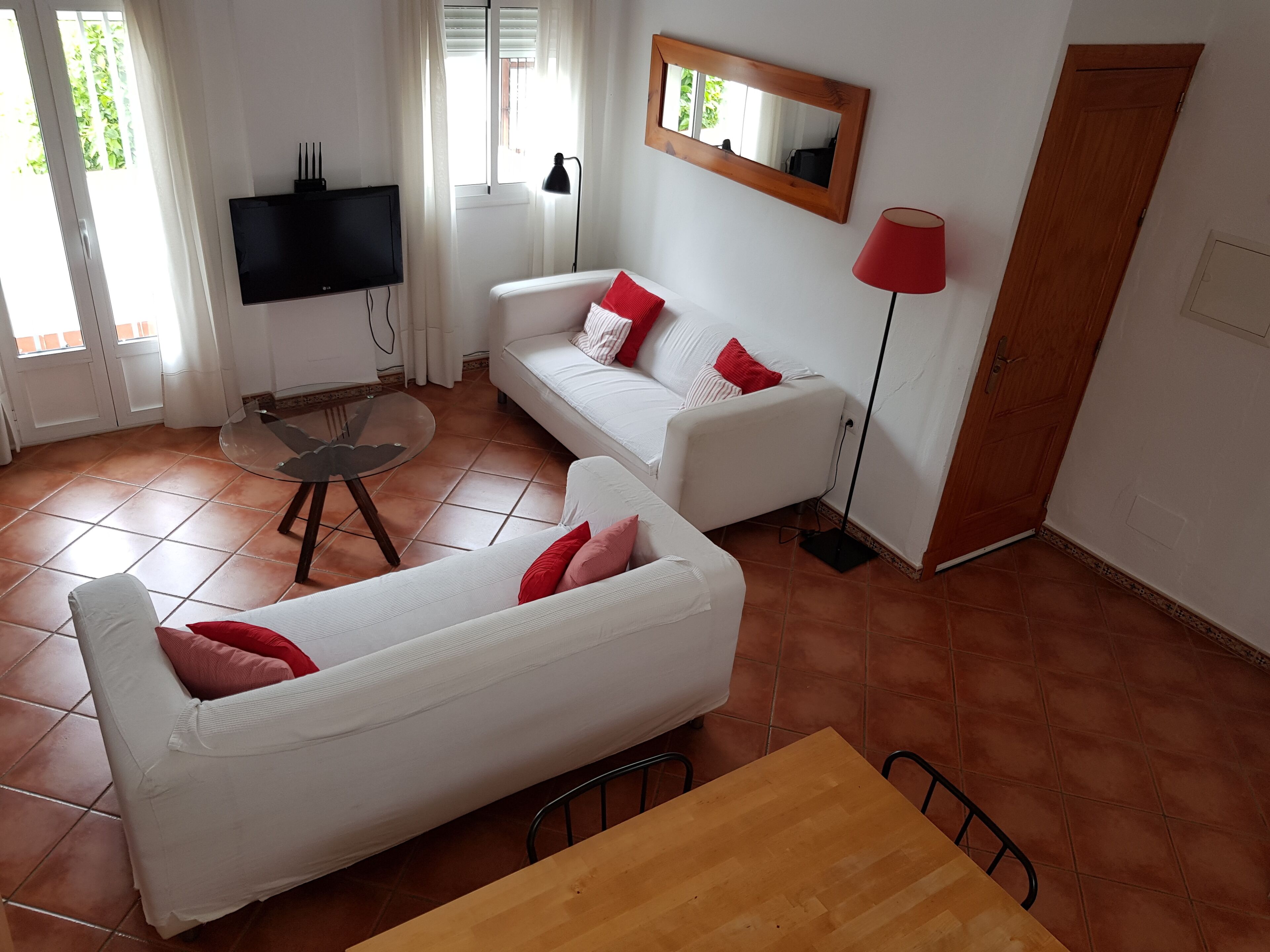 Een woonkamer met een witte bank, een houten tafel en een aan de muur bevestigde televisie.