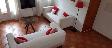 Een woonkamer met een witte bank, een houten tafel en een aan de muur bevestigde televisie.