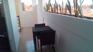 A small balcony with a table and chairs, a window with a view of buildings, and a plant on the wall. - Chic One bedroom serviced  apartment with  pool- fully self contained  V6 (Accra)