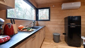 Una cucina compatta con pareti in legno, una finestra, un lavello, un bollitore rosso, un frigorifero nero e un cestino.