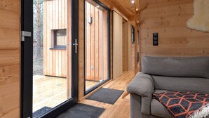 Un interno moderno con pavimento in legno, un divano grigio e un'ampia porta scorrevole in vetro che dà su uno spazio esterno.