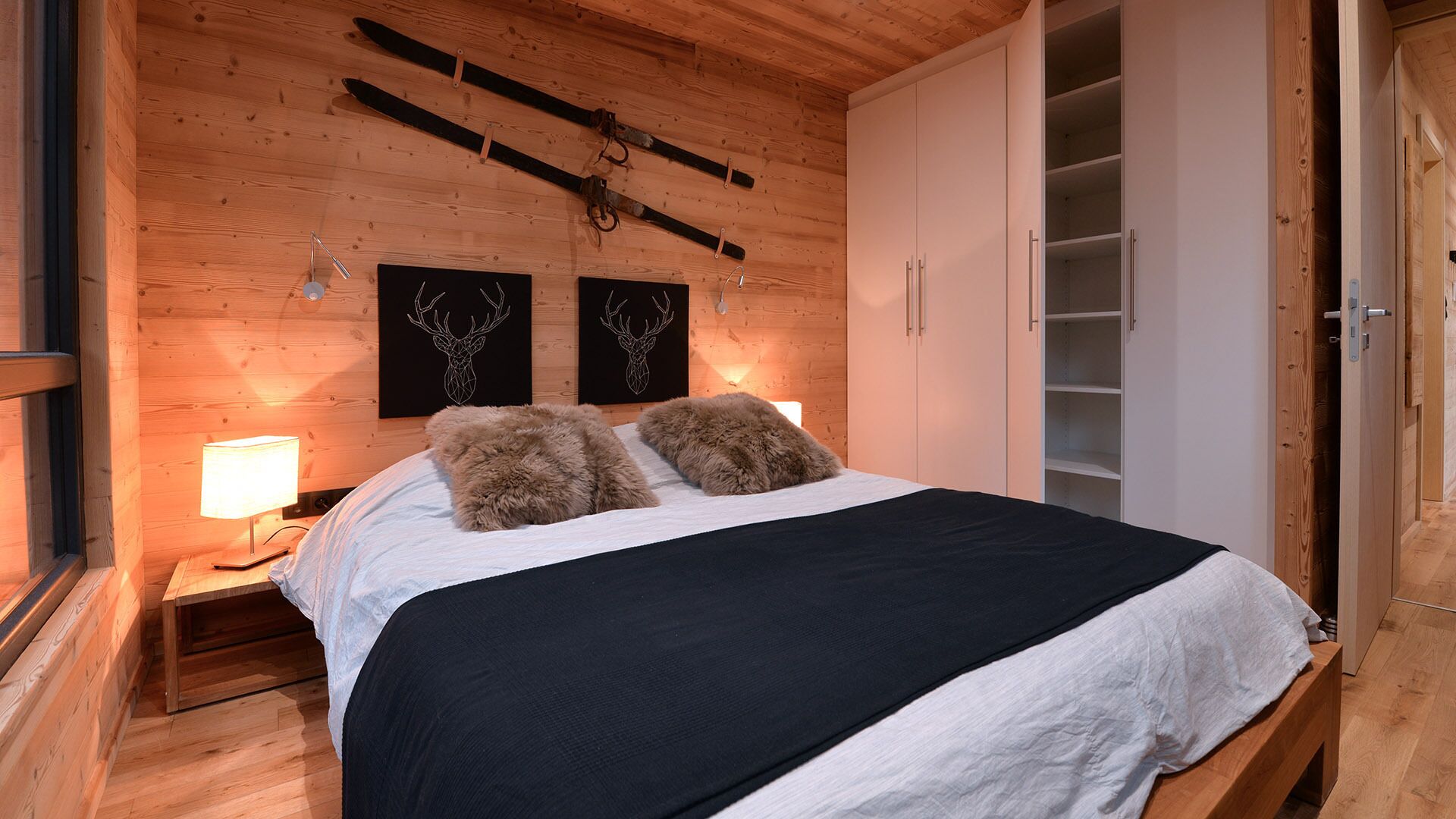 Une chambre à coucher aux murs lambrissés, avec un lit, deux décorations murales représentant des bois de cerf et une armoire.