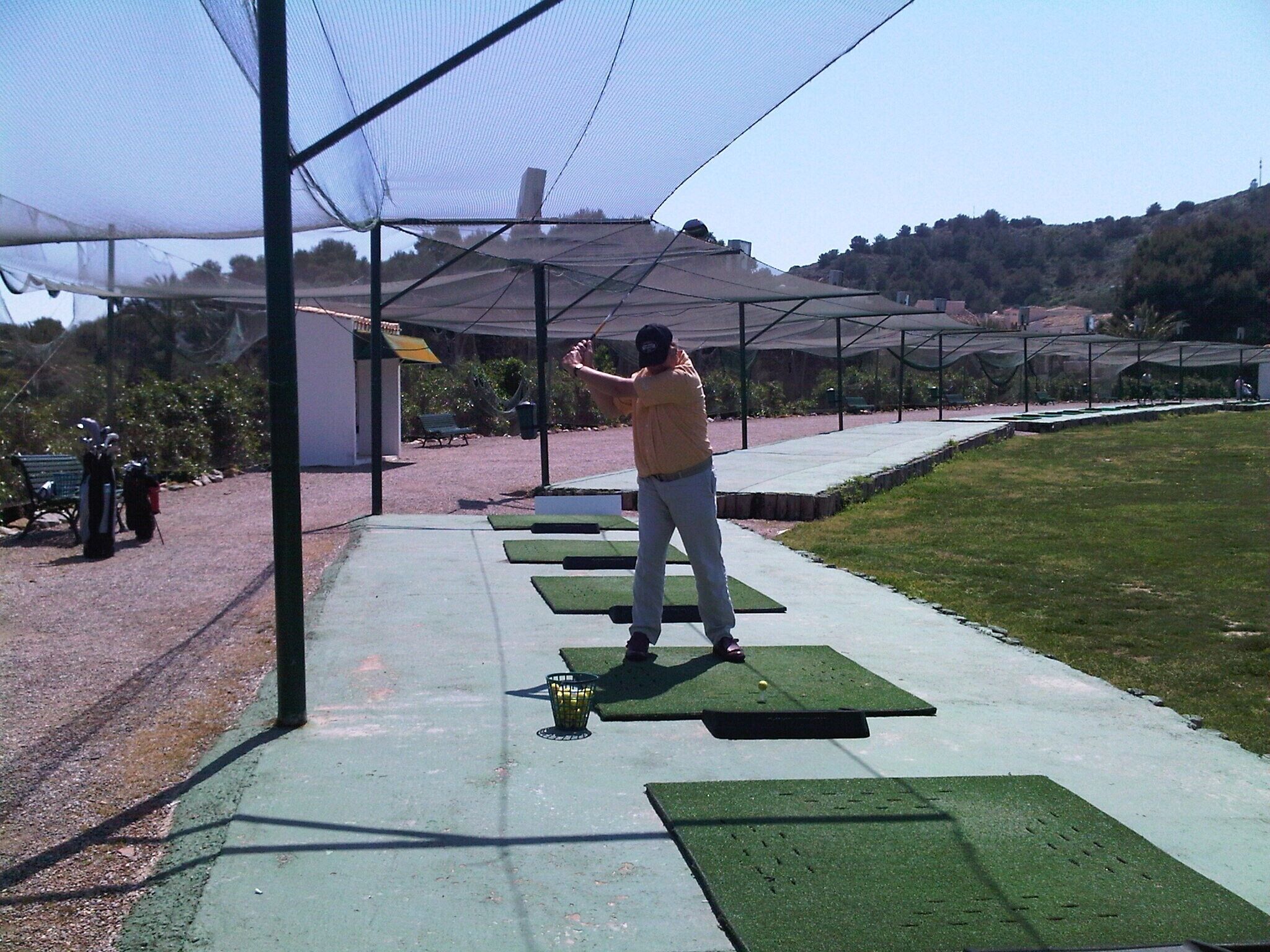 Une personne qui pratique le golf sur un tapis vert, à l’intérieur d’une structure recouverte de filets.