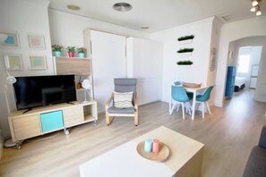 A modern living room with a TV, a dining area with chairs, a sofa, and a small table with candles.