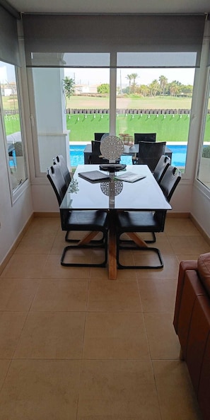 Un comedor con mesa y sillas, vista a una piscina y un patio con sofá de cuero marrón.