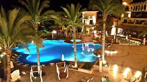 A nighttime view of a hotel pool area with palm trees, lounge chairs, and a building in the background. - Great Frontline Golf Villa With Private Pool And Free Wi-Fi (Torre Pacheco)