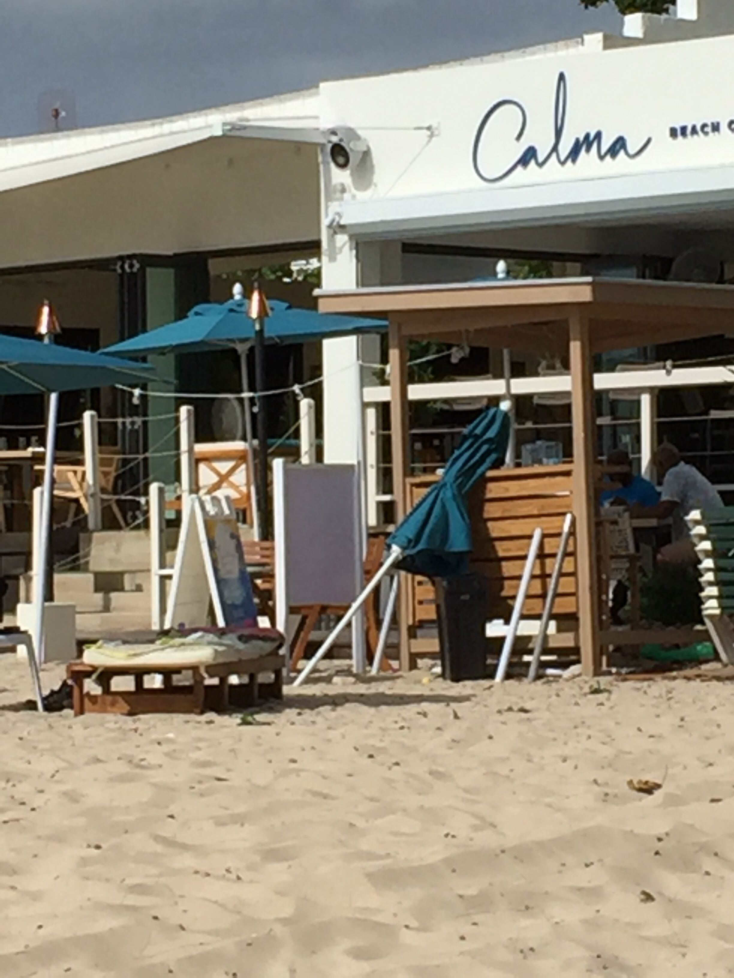 A beachside cafe named 'Calma Beach' with outdoor seating and umbrellas.