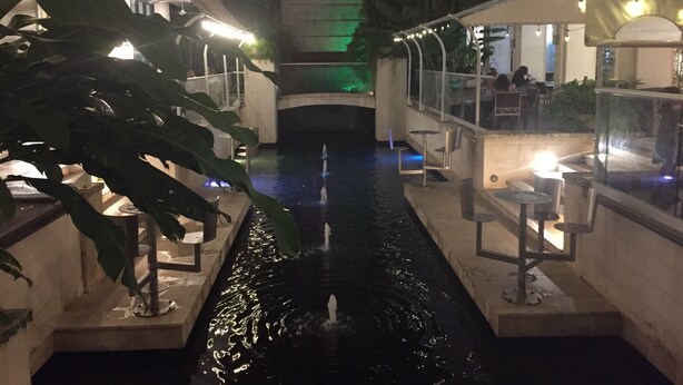 Ein Zimmerbrunnen mit Sitzgelegenheiten und Pflanzen, umgeben von Wänden und einer Treppe.