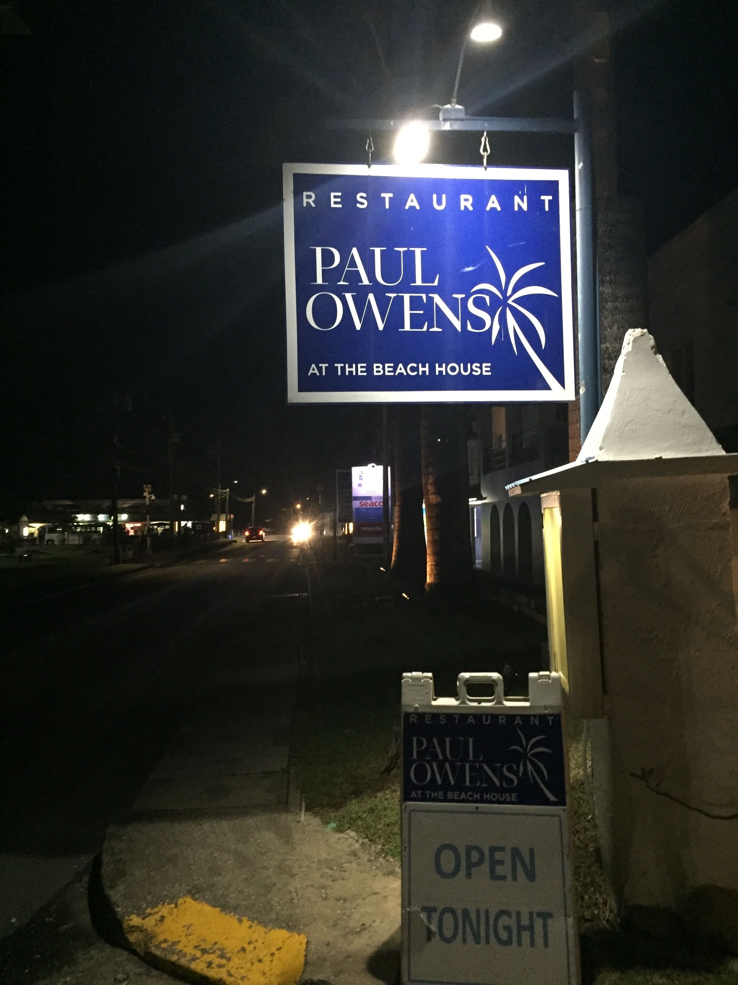 En restaurangskylt för ”Paul Owens at the Beach House”, med en skylt under som visar ”ÖPPET IK VÄLL”.
