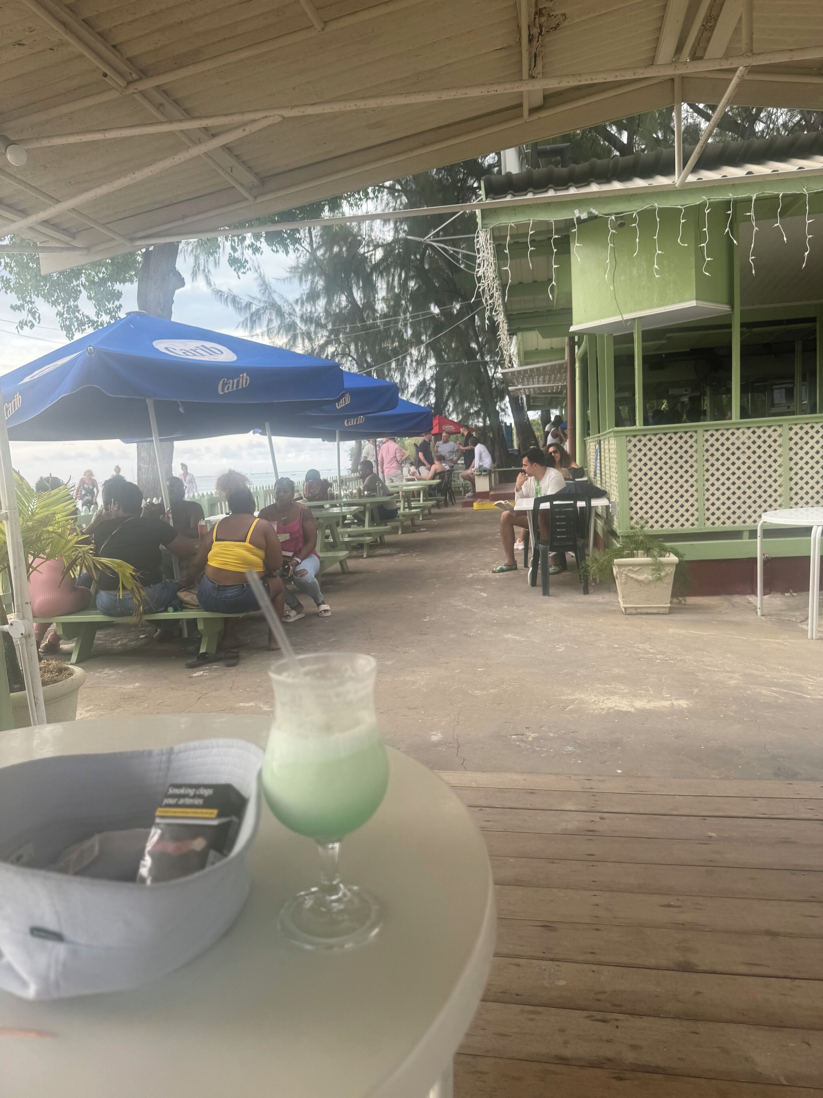 An outdoor seating area with tables and chairs under a covered roof, some with umbrellas.