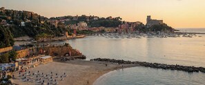 A coastal cityscape with a beach, rocky shoreline, and historic buildings.