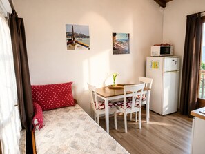 Une petite pièce comprenant un lit, une table à manger avec des chaises, un réfrigérateur et deux tableaux accrochés au mur.