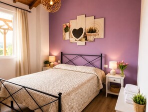 Une chambre à coucher comprenant un lit, des tables de chevet, une œuvre d’art accrochée au mur, une fenêtre avec des rideaux et un plafond en bois.
