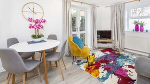 A modern living room with a round table, chairs, a TV, and a colorful rug. - Minster's Reach Holiday Apartment (YORK)