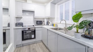 A modern kitchen with white cabinets, a microwave, an oven, and a sink. - Minster's Reach Holiday Apartment (YORK)