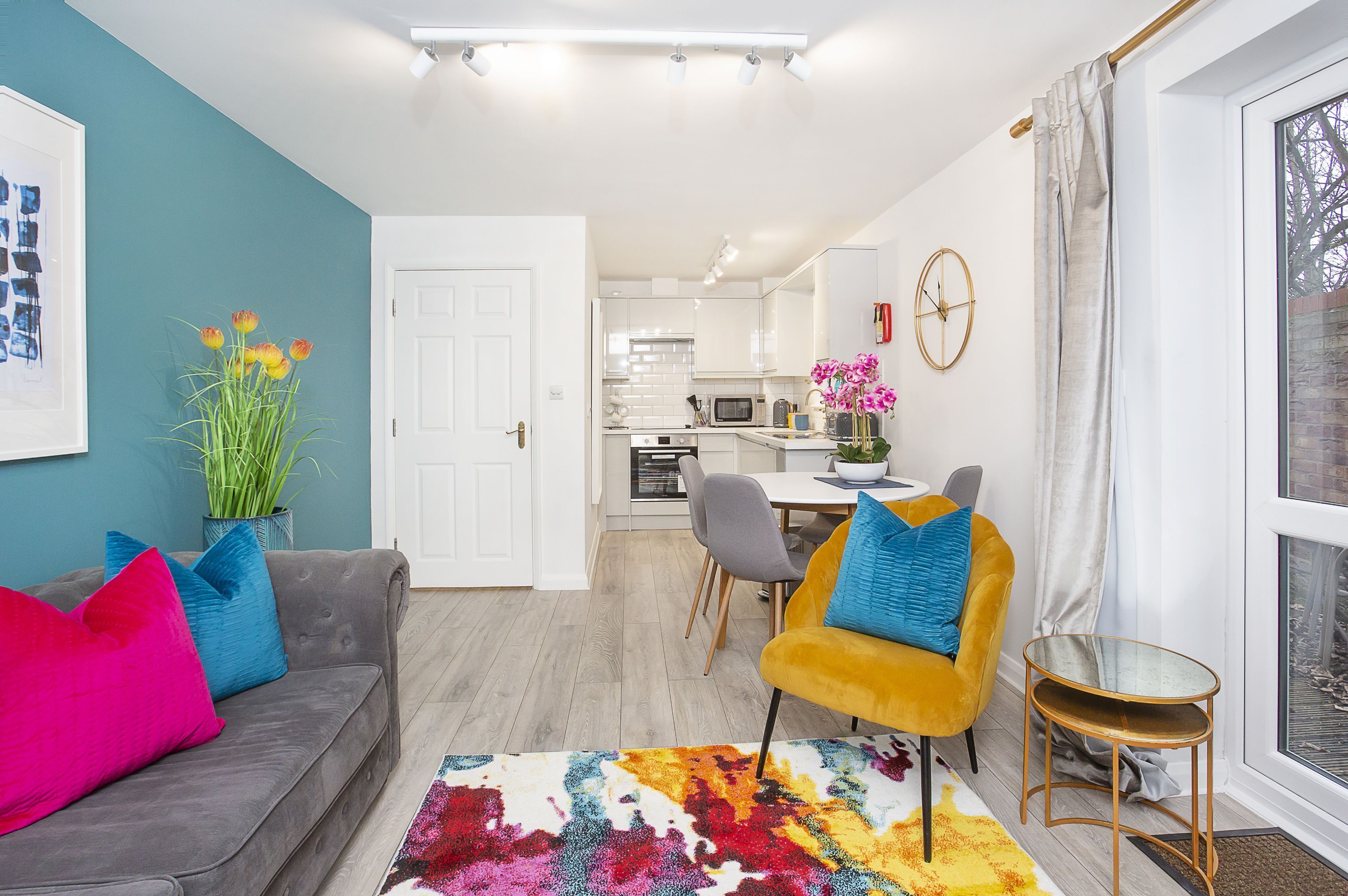 A modern living room with a sofa, a vibrant rug, and a dining area with a table and chairs.