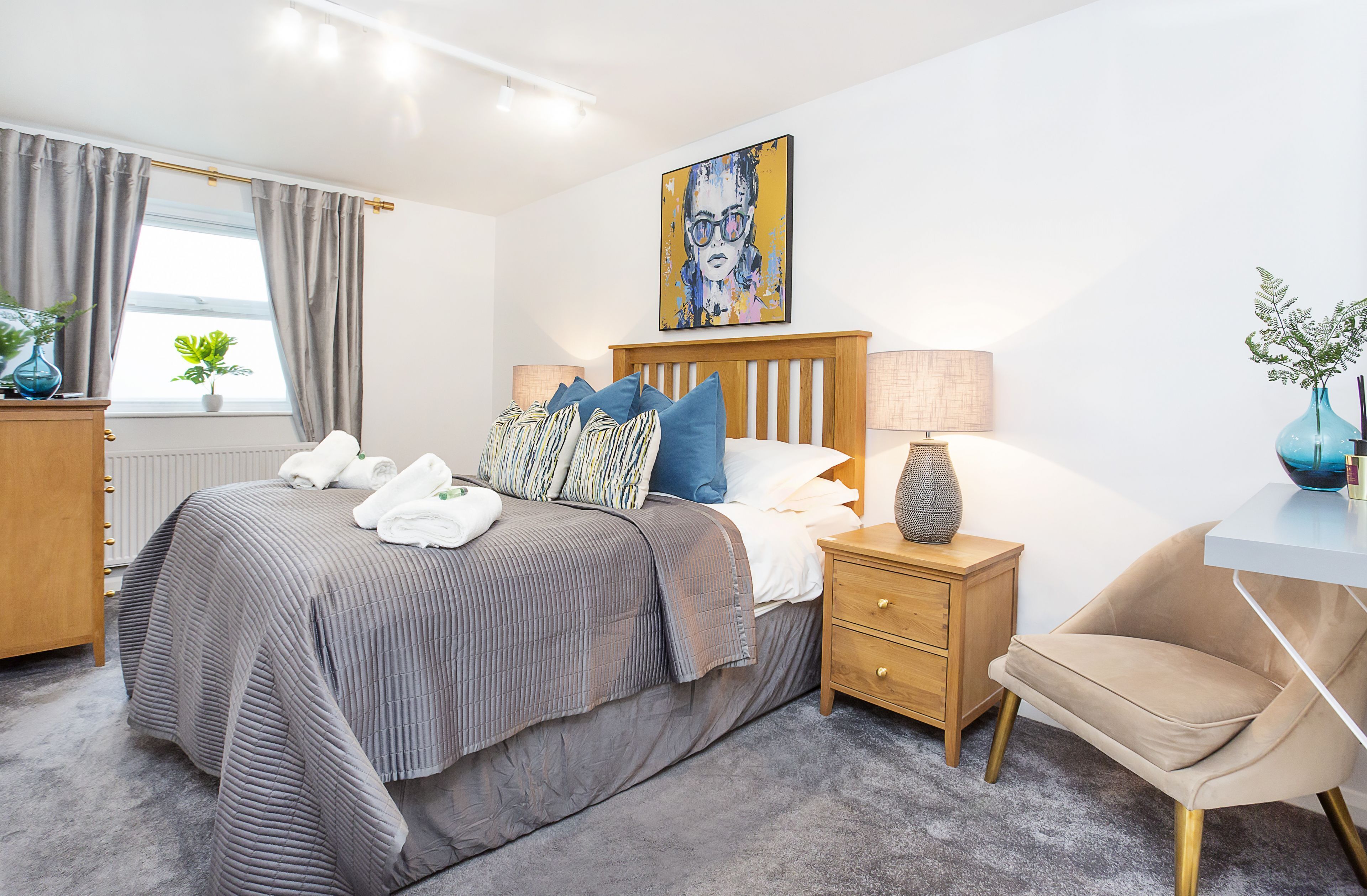A modern bedroom with a bed, bedside tables, a chair, and a painting on the wall.