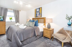 Une chambre à coucher moderne avec un lit, des tables de chevet, une chaise et un tableau au mur.