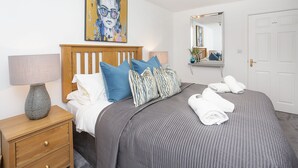 A neatly made bed with a grey quilt, blue and striped pillows, and white towels. - Minster's Reach Holiday Apartment (YORK)