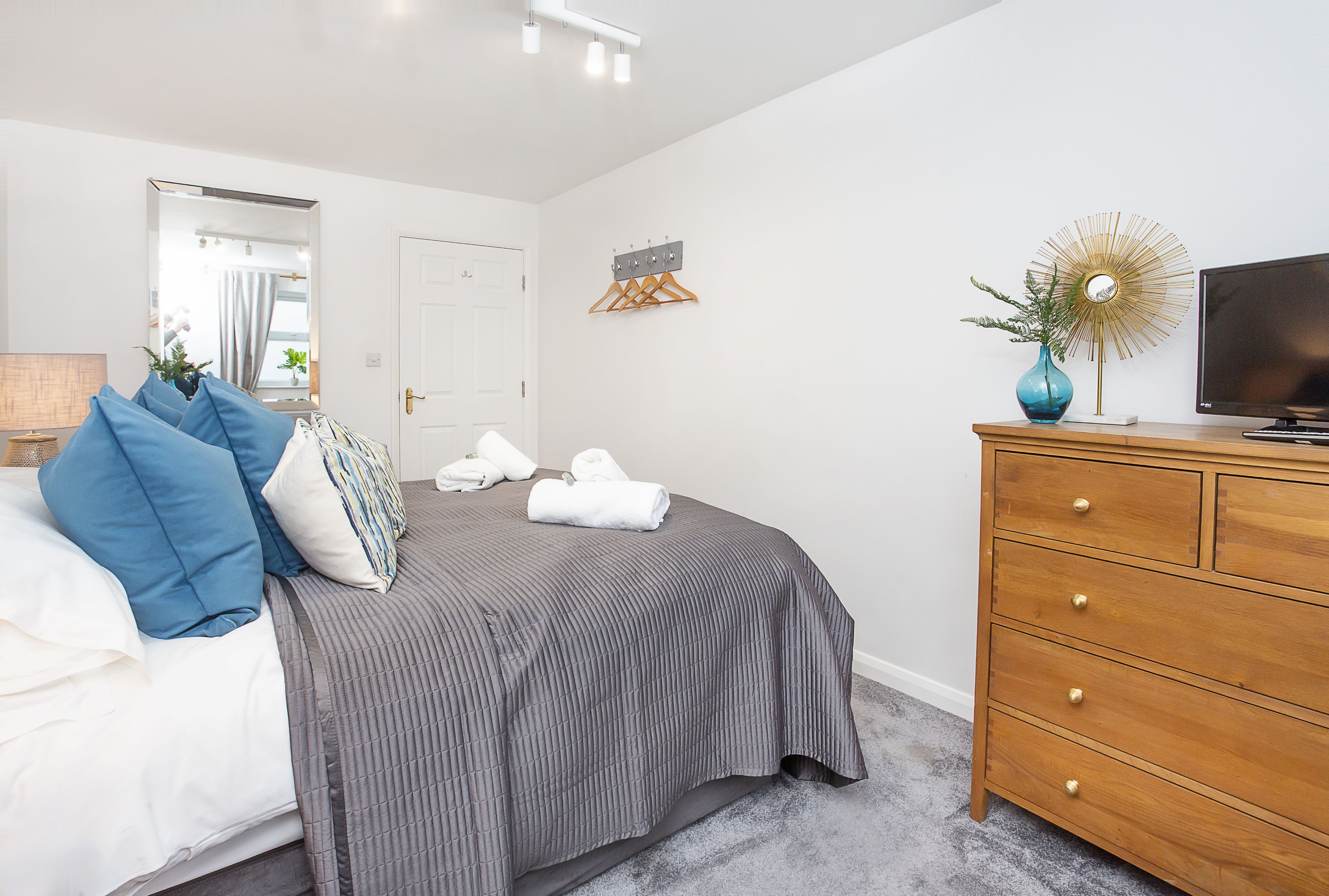 A bedroom with a bed, a dresser, a television, and a mirror.