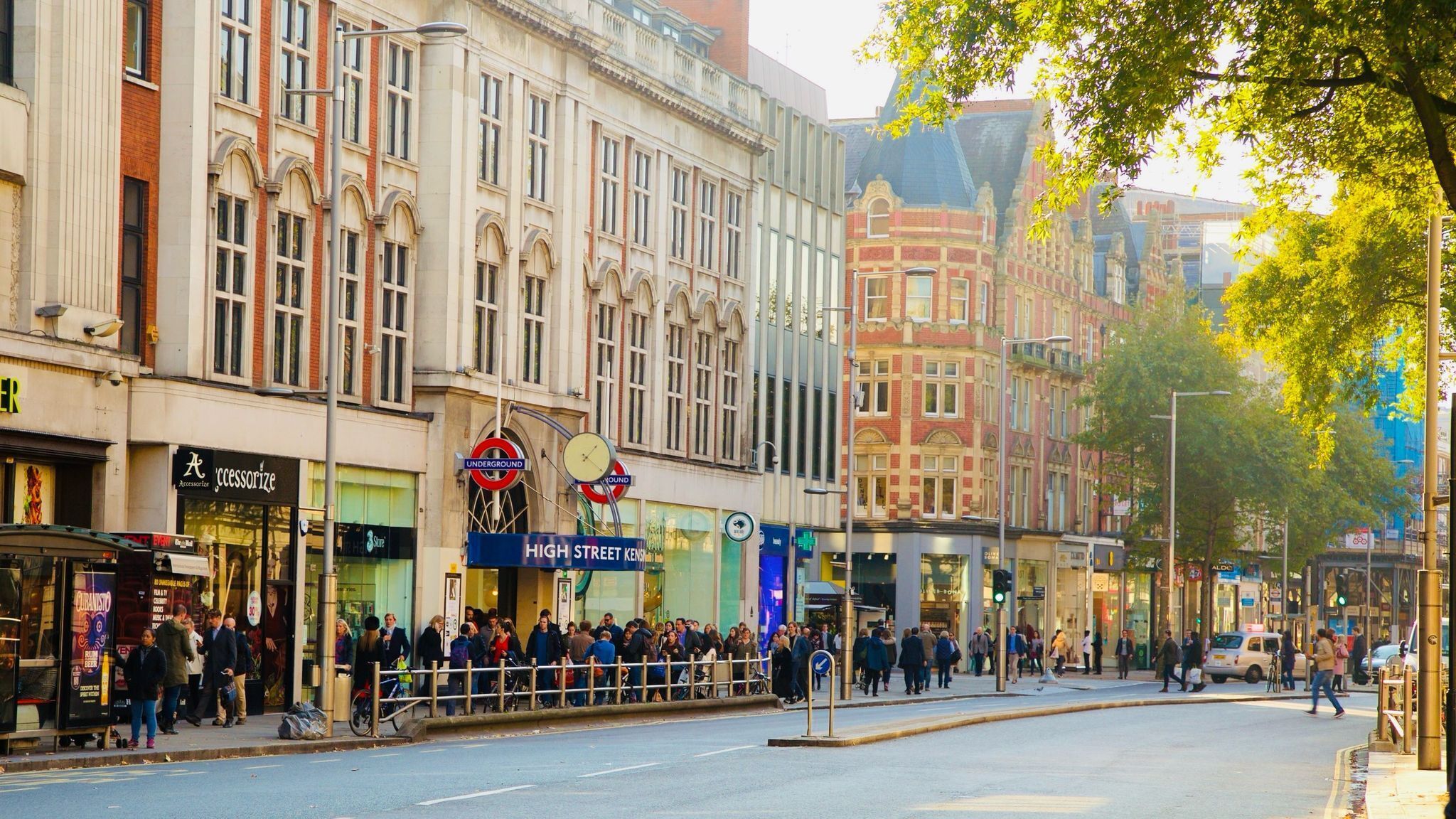 Eine Straße mit einer Menschenmenge in der Nähe eines Gebäudes, das ein Schild für 'High Street Kenzie' zeigt.