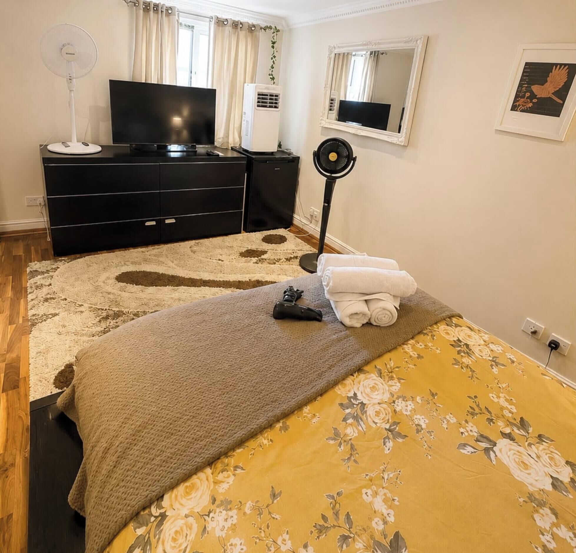 A bedroom with a bed, a dresser, a TV, an air conditioner, and a fan.