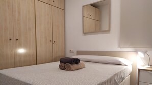 Una cama bien hecha con una colcha estampada, una lámpara de noche y un armario de madera con dos puertas.
